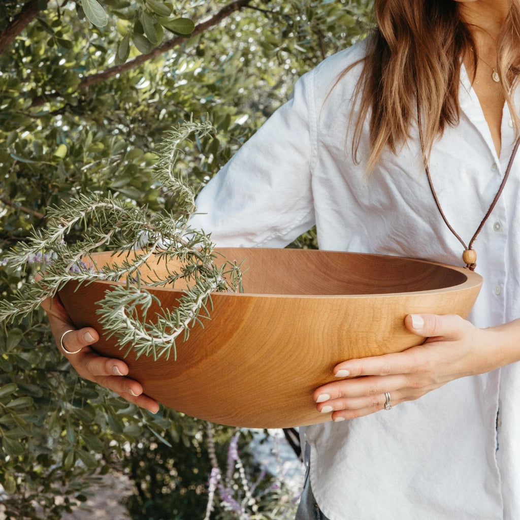 woman wearing hat holding large wood salad bowl with rosemary outside