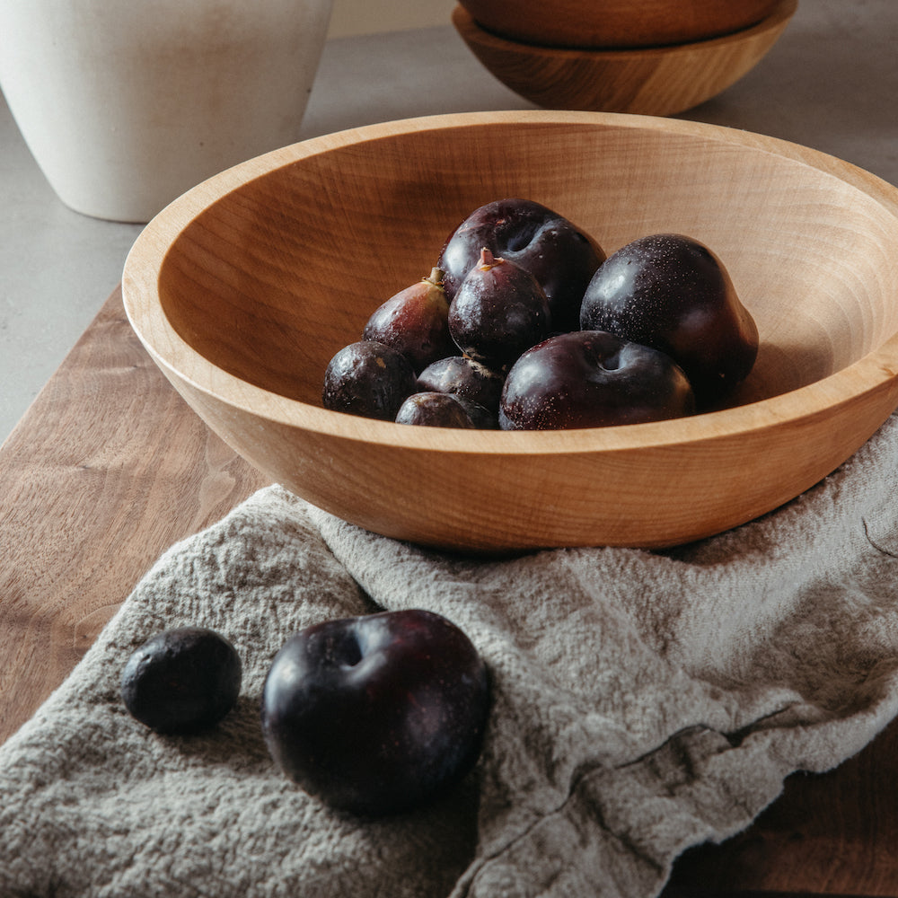 large wood salad bowl on oversized linen napkins with plums and figs