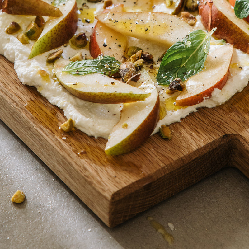 wooden serving board with ricotta pears pistachios honey and mint