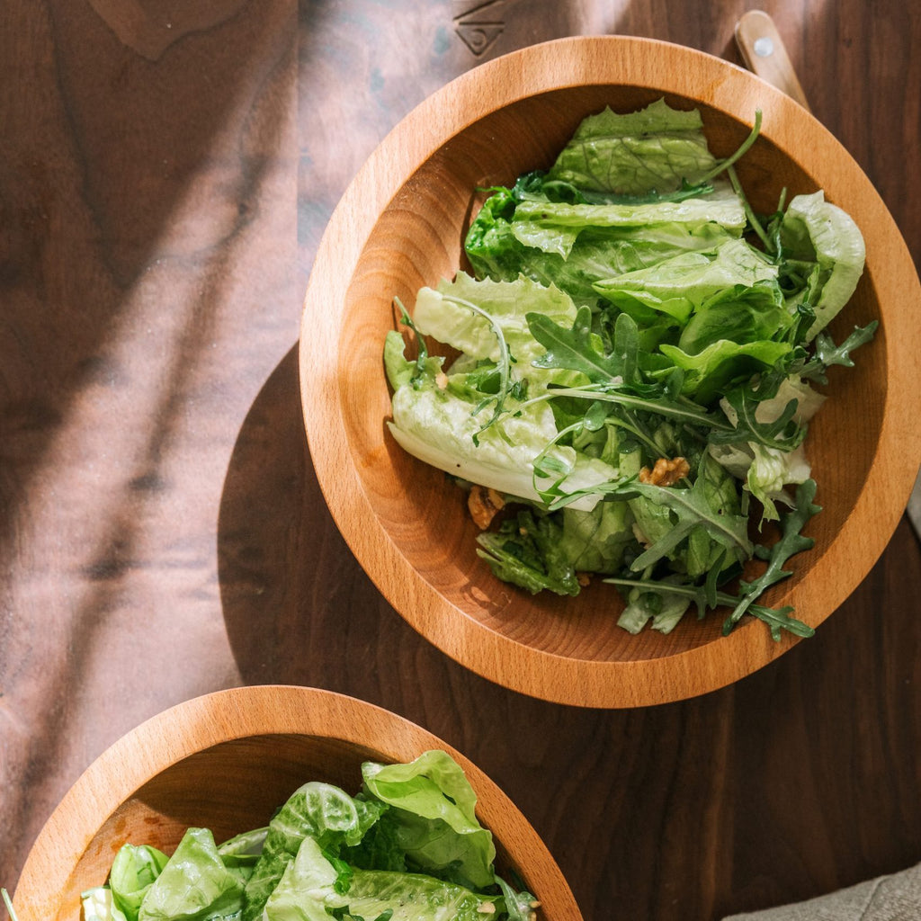 wooden salad bowl set with green salad on wooden serving board