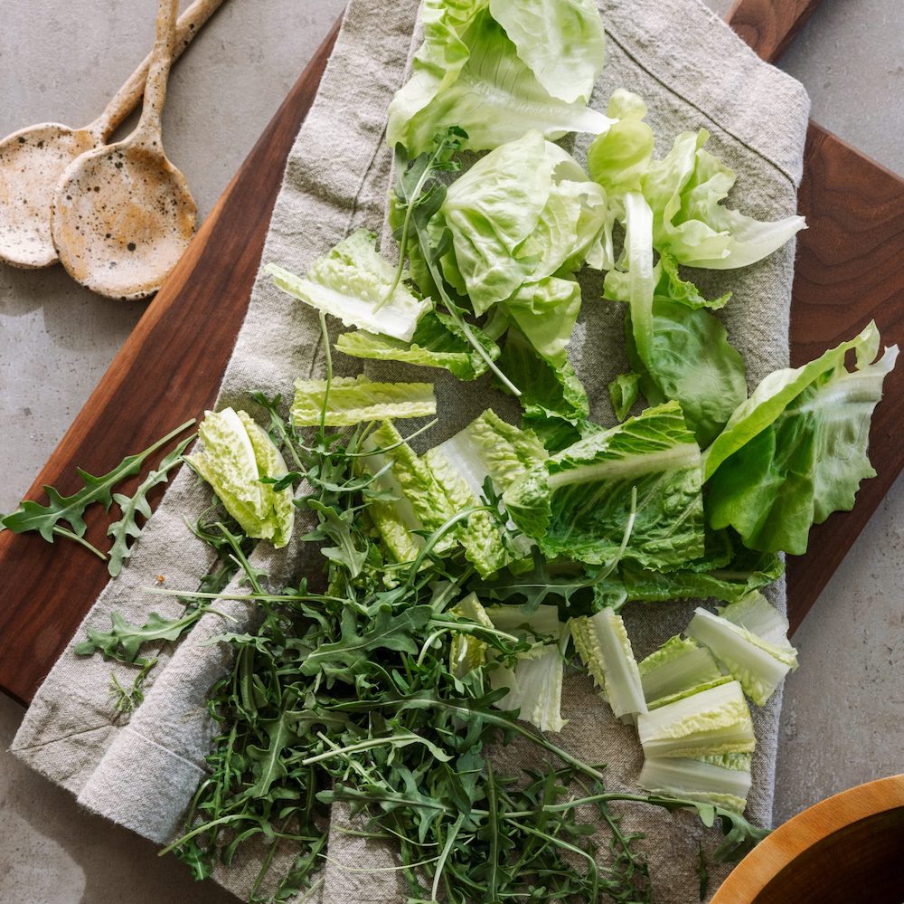 large oversized linen napkins on wooden serving board with lettuce and greens