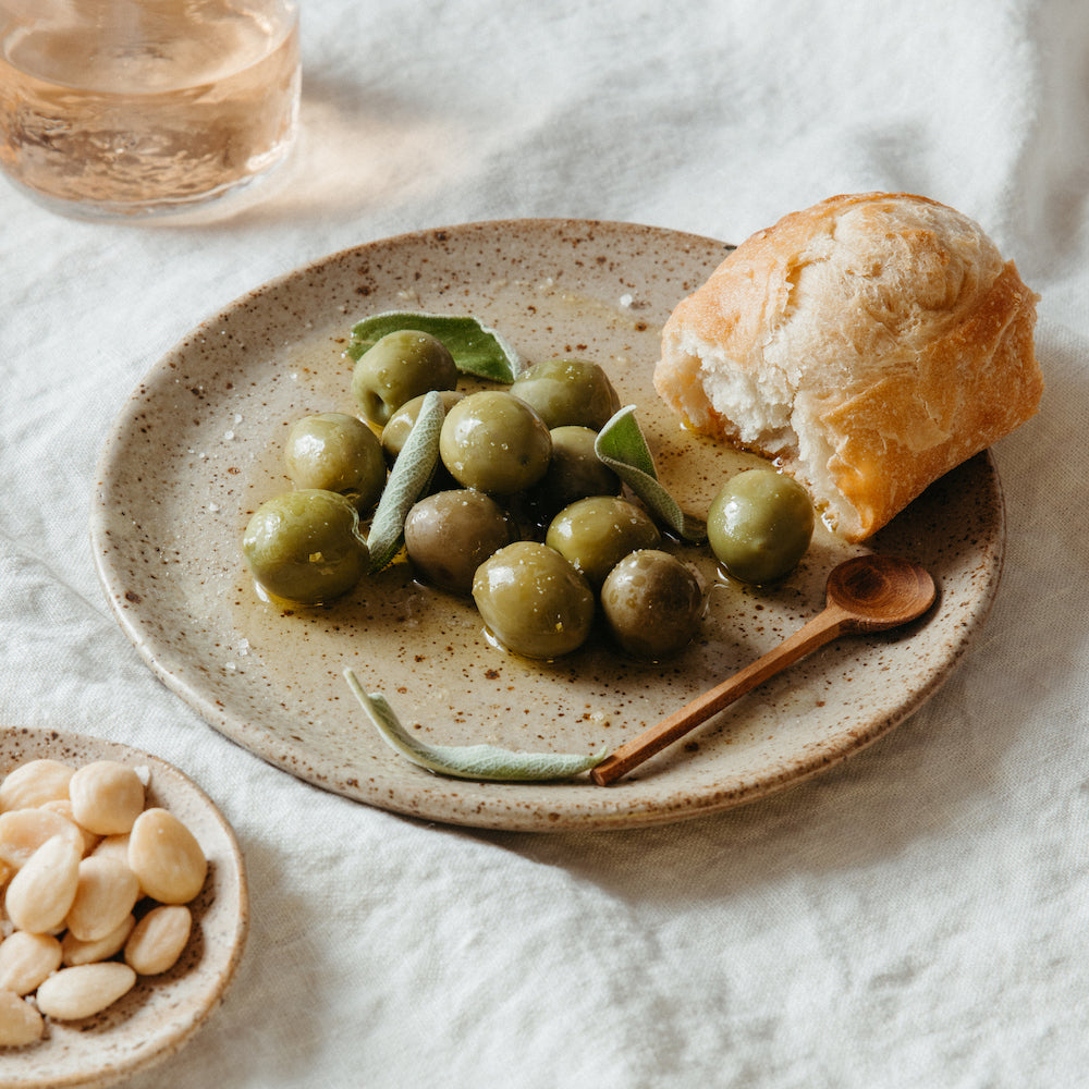 wooden salt spoons on stoneware salad plates with bread olives marcona almonds and sage