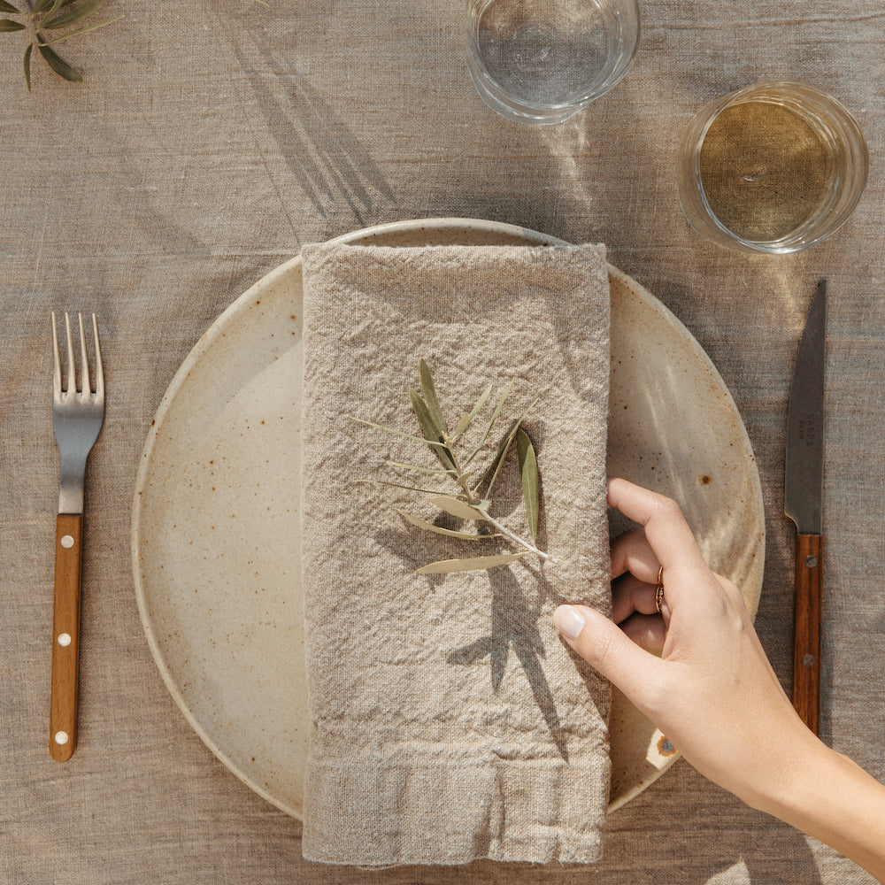 Sabre cutlery flatware on stoneware dinner plates with oversized linen napkins and herbs